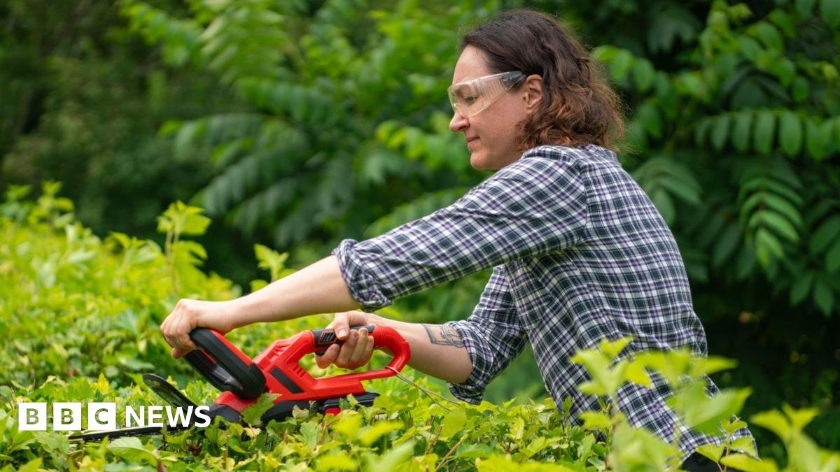 A woman trims a hedge whilst wearing goggles